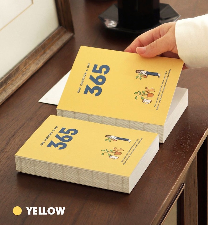 May include: A yellow journal with the text "ONE QUESTION A DAY 365" on the cover. The journal is closed and stacked on top of another identical journal.