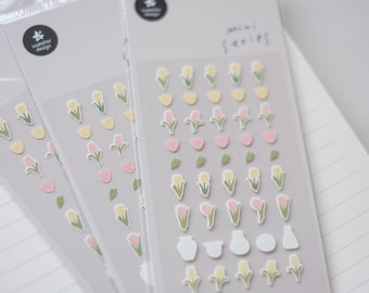 May include: Three sheets of stickers with a variety of floral designs. The stickers feature pink, yellow, and green flowers, as well as small white vases. The text "mini series" is printed on the top sheet.
