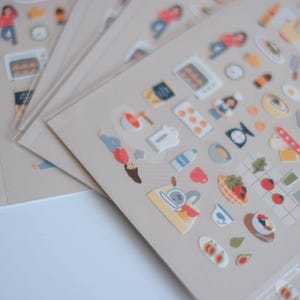 May include: Sheets of stickers featuring various kitchen and cooking-related illustrations. The stickers include images of food, kitchen appliances, and people. The stickers are in a variety of colors, including red, blue, and yellow.