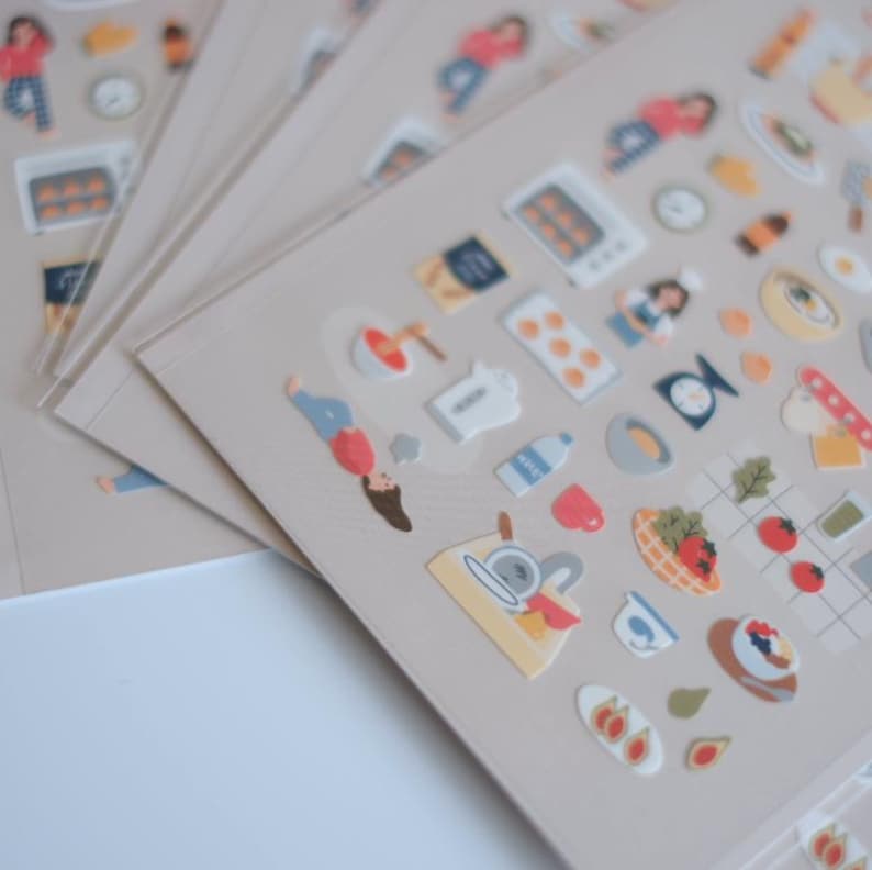 May include: Sheets of stickers featuring various kitchen and cooking-related illustrations. The stickers include images of food, kitchen appliances, and people. The stickers are in a variety of colors, including red, blue, and yellow.