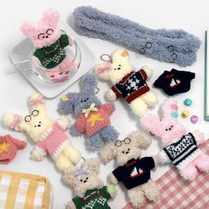 May include: A collection of eight plush toys, each wearing a different knitted sweater. The sweaters feature various patterns, including snowflakes, stripes, and stars. The toys are made of soft, fluffy material and are perfect for cuddling.