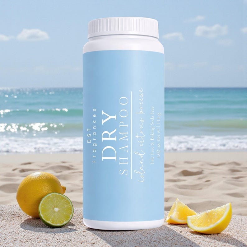 May include: A white and light blue dry shampoo bottle with the text "DRY SHAMPOO" and "Island citrus breeze". The bottle is on a sandy beach with lemons and limes. The ocean is in the background.