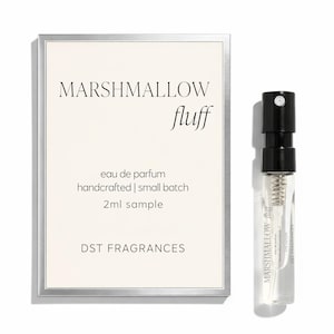 May include: A sample of "Marshmallow Fluff" eau de parfum. The clear glass vial has a black cap and contains a small amount of liquid. A white card with silver trim displays the fragrance name, details, and brand name. The card reads "eau de parfum, handcrafted | small batch, 2ml sample."