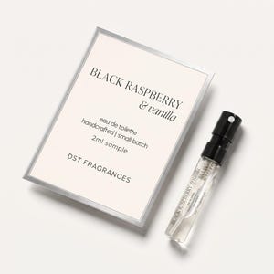 May include: A 2ml sample of Black Raspberry & Vanilla eau de toilette by DST Fragrances. The product includes a small clear glass spray vial with a black cap and a rectangular card featuring the product name, scent, and brand information.