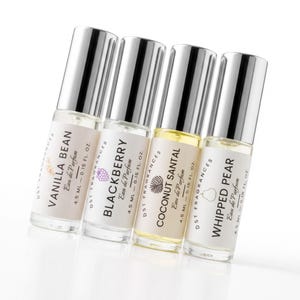 May include: Four clear glass rollerball perfume bottles with silver caps, each containing 4.5 ml or 0.15 fl. oz. of liquid. The labels are printed with DST FRAGRANCES and the scents Vanilla Bean, Blackberry, Coconut Santal, and Whipped Pear.