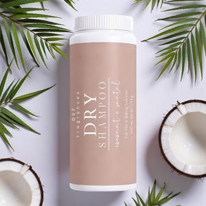May include: A white and tan dry shampoo bottle with the text "DRY SHAMPOO coconut + santal". The bottle is surrounded by green palm leaves and coconut halves. The bottle contains 4.02 oz. net wt | 114 g.