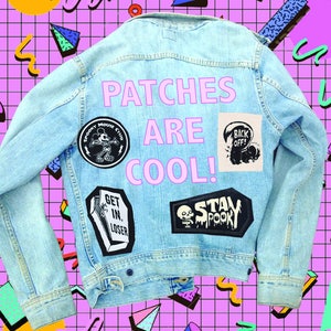 May include: A light blue denim jacket with various patches, including a Mickey Mouse patch, a skull and crossbones patch, and a "Stay Spooky" patch. The text "Patches Are Cool!" is written in pink on the back of the jacket.