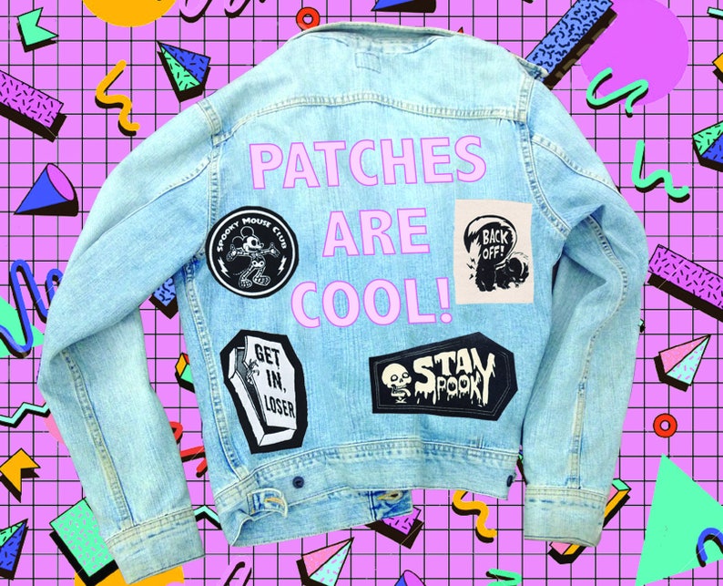 May include: A light blue denim jacket with various patches, including a Mickey Mouse patch, a skull and crossbones patch, and a "Stay Spooky" patch. The text "Patches Are Cool!" is written in pink on the back of the jacket.