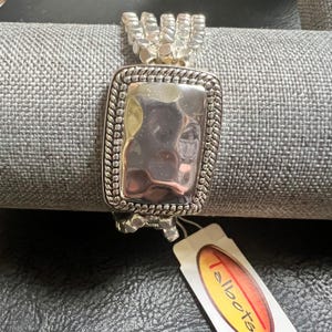 May include: Silver-toned bracelet with a hammered rectangular center piece. The bracelet has a braided border and a series of small, textured links. A Talbots tag is attached.