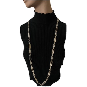 May include: A long gold-tone chain necklace featuring alternating rectangular links and small circular links. The necklace is displayed on a black ribbed mock neck top. The design consists of a repeating pattern of elongated rectangular metal links connected by smaller, textured circular rings throughout the entire length of the chain.