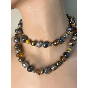 May include: A two-strand necklace featuring a mix of beads in silver, brown, yellow, and clear amber tones. The beads vary in size and texture, creating a layered effect. The necklace is displayed on a mannequin.