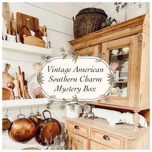 Puede incluir: Una alacena de madera con puertas de cristal, estantes con tablas de cortar de madera y sartenes de cobre colgadas debajo. Una etiqueta central muestra el texto Vintage American Southern Charm Mystery Box con una ilustración floral.