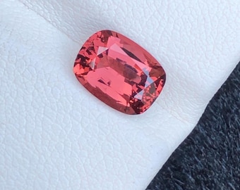 May include: A vibrant pink gemstone with a cushion cut. The gemstone is set against a white background.