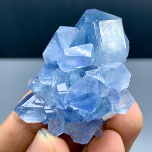 以下が含まれることがあります： シャープな幾何学的な形をした、明るい青色の結晶のクラスター。結晶は半透明で、さまざまな青色の濃淡があります。全体的な形状は不規則で、複数の結晶のポイントがあります。背景は濃い青色です。