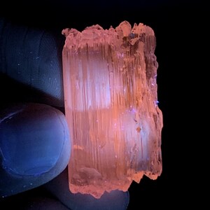 Peut inclure: Un cristal translucide rose et orange avec des stries. Le cristal est &eacute;clair&eacute; par une lumi&egrave;re UV, ce qui le fait briller.
