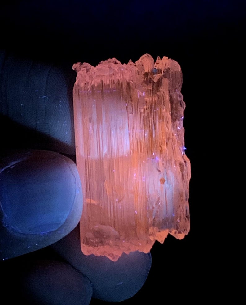 Peut inclure: Un cristal translucide rose et orange avec des stries. Le cristal est &eacute;clair&eacute; par une lumi&egrave;re UV, ce qui le fait briller.