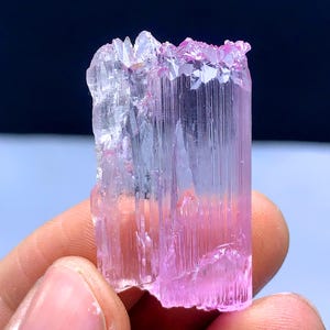Peut inclure: Un cristal allong&eacute; facett&eacute;, rose et transparent, avec des stries. Le cristal est translucide et pr&eacute;sente une l&eacute;g&egrave;re teinte rose.