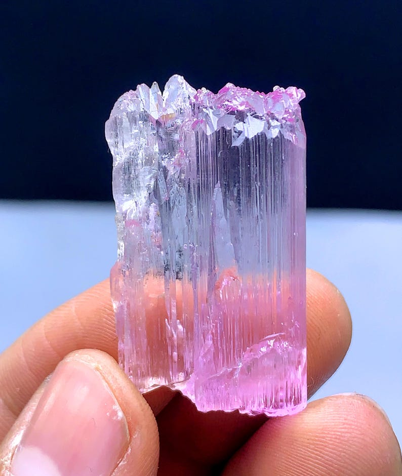 Peut inclure: Un cristal allong&eacute; facett&eacute;, rose et transparent, avec des stries. Le cristal est translucide et pr&eacute;sente une l&eacute;g&egrave;re teinte rose.