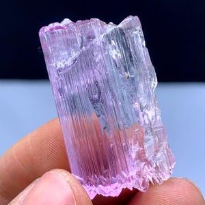 Peut inclure: Un cristal allong&eacute; facett&eacute; rose et transparent avec des stries. Le cristal est translucide et a une l&eacute;g&egrave;re teinte rose.