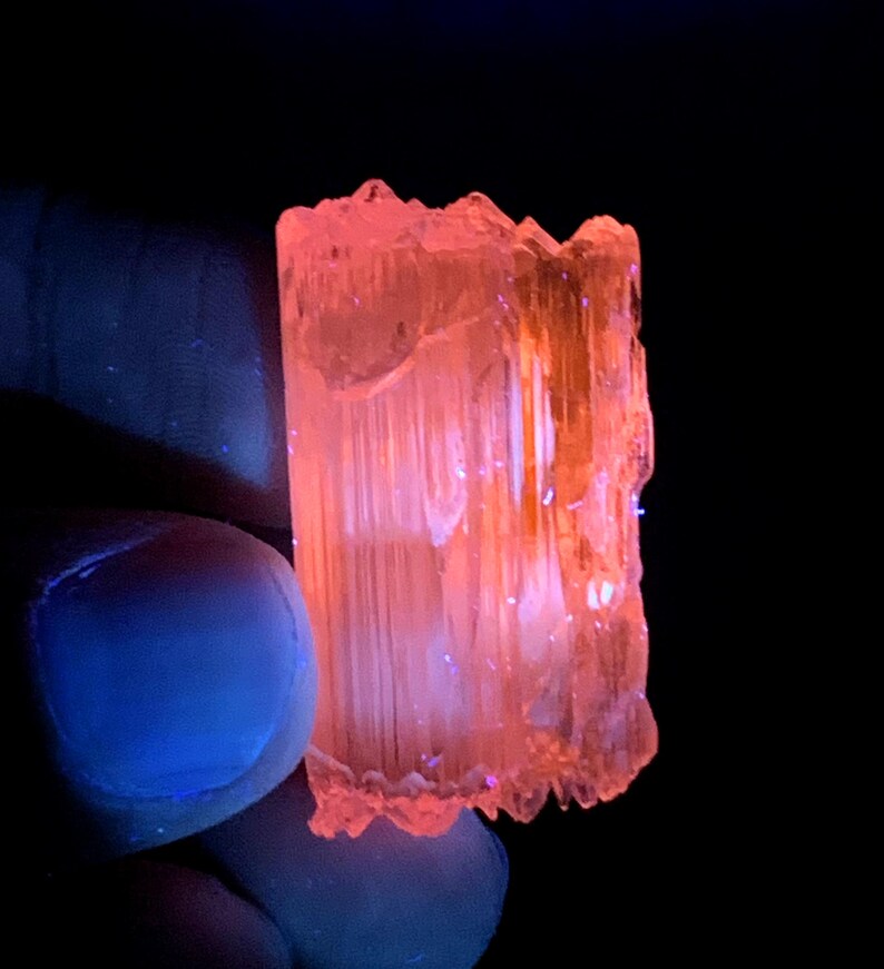 Peut inclure: Un cristal translucide orange-rose avec une texture stri&eacute;e. Le cristal est &eacute;clair&eacute; par une lumi&egrave;re UV, ce qui le fait briller intens&eacute;ment.