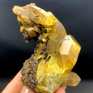 May include: A cluster of yellow calcite crystals with a brown matrix. The crystals are sharp and well-defined, with a glassy luster. The matrix is rough and textured.