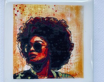 May include: Square ceramic tile featuring a stylized portrait of a person with sunglasses and a large afro. The portrait is set against a textured orange and yellow background. The text "Am I Next" is printed at the bottom of the tile.