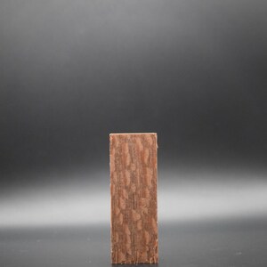 May include: A close-up of a rectangular piece of wood with a brown and reddish-brown wood grain pattern.