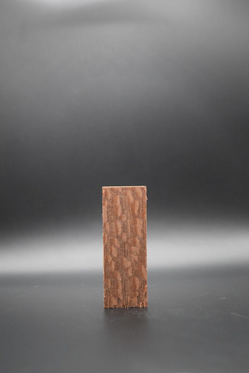 May include: A close-up of a rectangular piece of wood with a brown and reddish-brown wood grain pattern.