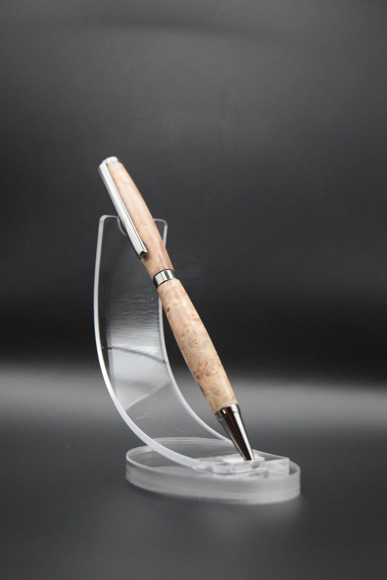 Op de afbeelding: Een houten pen met een zilveren rand, getoond op een transparante kunststof standaard. De pen heeft een lichtbruine kleur met donkerbruine swirls.