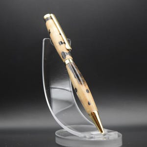 May include: A wooden pen with a gold-colored top and a black and brown wood grain pattern. The pen is displayed on a clear plastic stand.