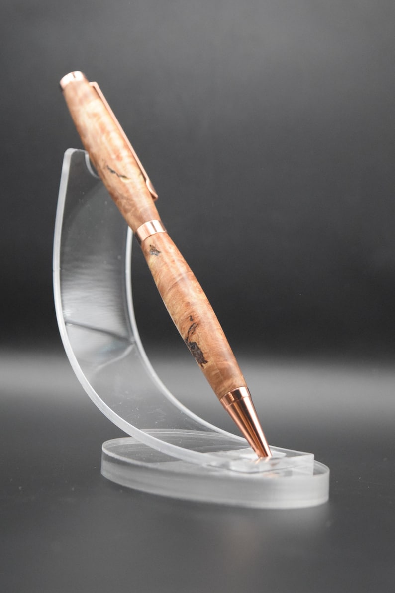 May include: A handcrafted wooden pen with copper-colored accents. The pen features a light brown, burl wood grain pattern and is displayed on a clear acrylic stand. The pen's tip, clip, and bands are copper-colored.