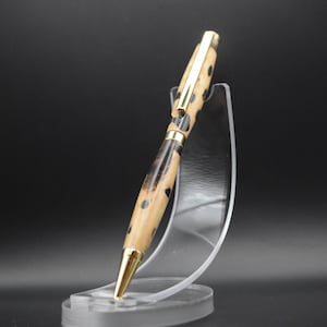 May include: A wooden pen with a black and brown patterned design and gold accents. The pen is displayed on a clear plastic stand.