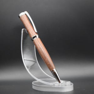 May include: A wooden pen with a silver trim, displayed on a clear plastic stand. The pen has a dark brown wood grain pattern.