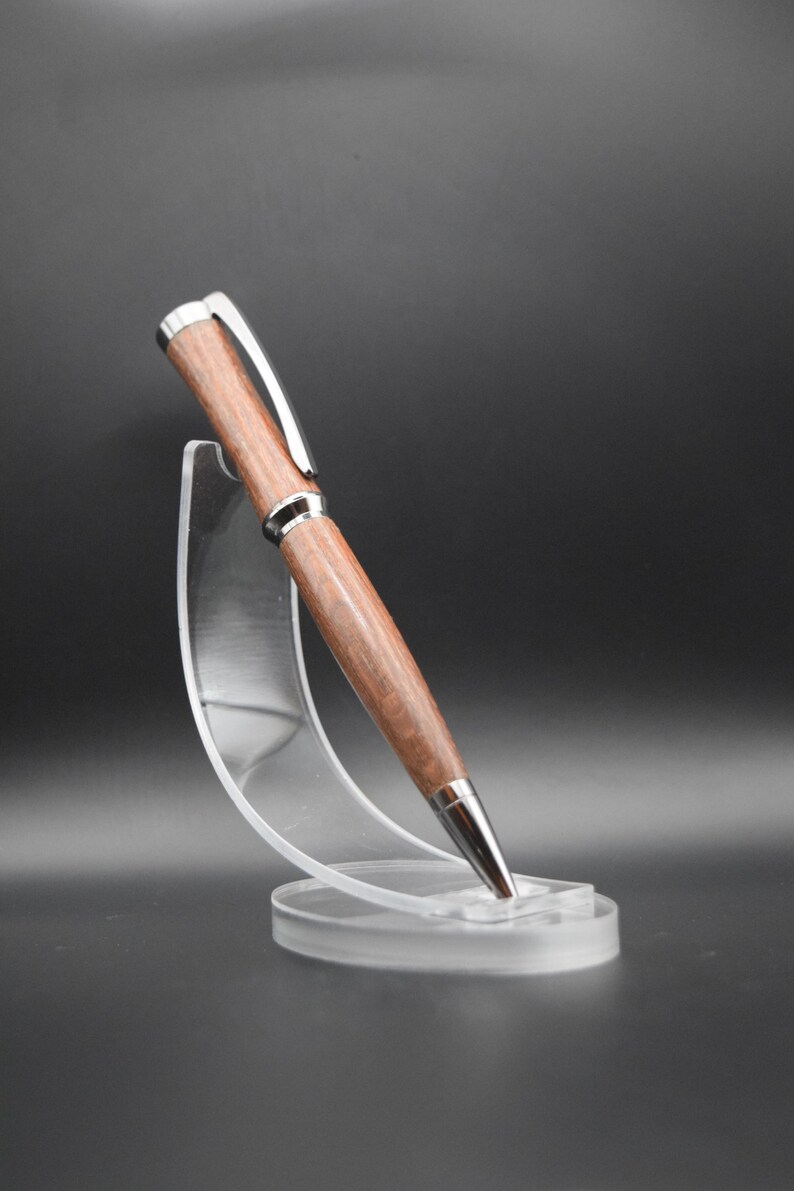 May include: A wooden pen with a silver trim, displayed on a clear plastic stand. The pen has a dark brown wood grain pattern.