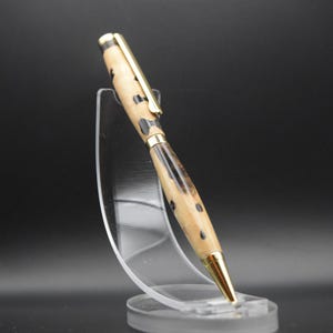 May include: A wooden pen with a black and brown wood grain pattern and a gold-colored metal top and bottom. The pen is displayed on a clear plastic stand.