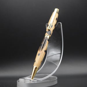 May include: A wooden pen with a black and brown patterned design and gold accents. The pen is displayed on a clear plastic stand.