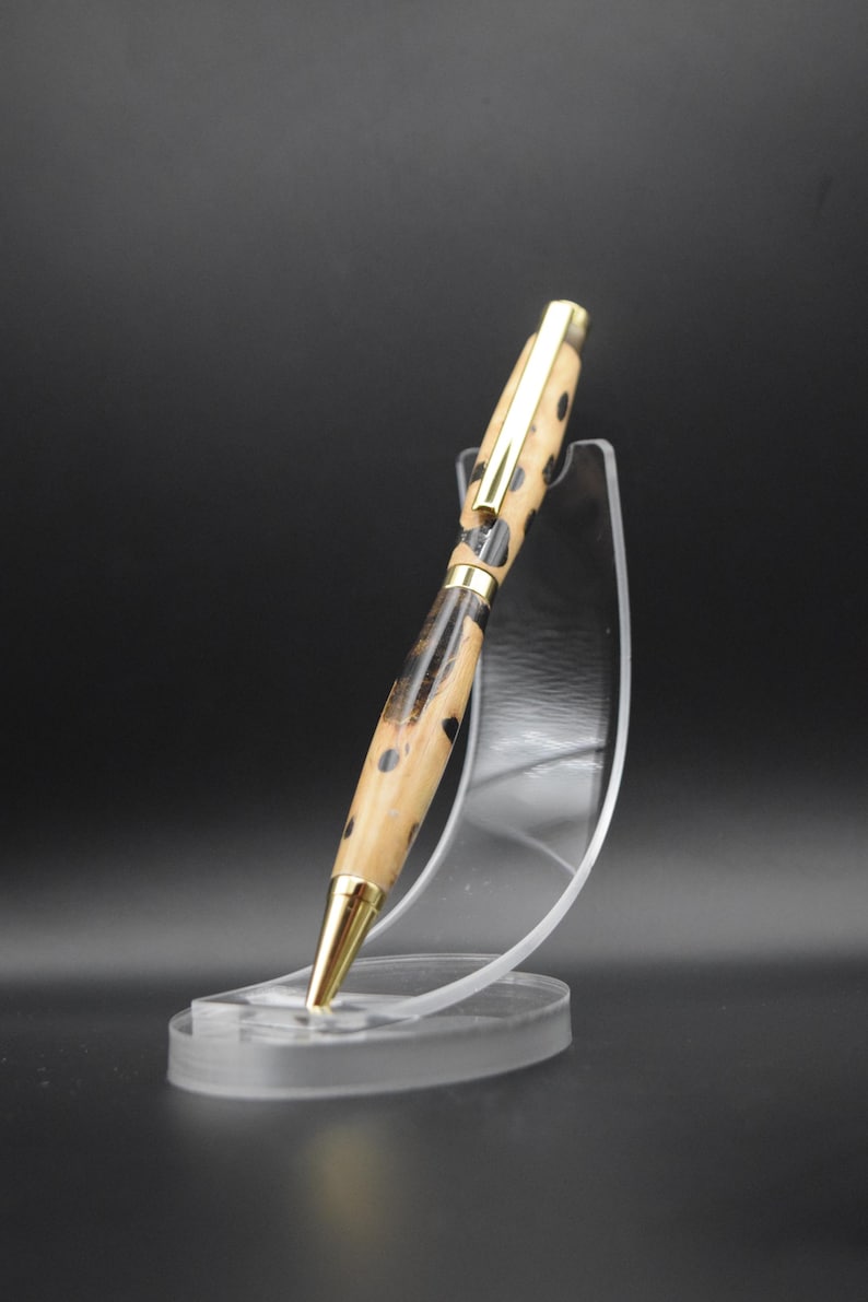 May include: A wooden pen with a black and brown patterned design and gold accents. The pen is displayed on a clear plastic stand.