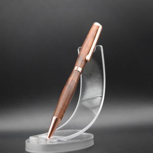 May include: A wooden pen with a rose gold finish and a clear plastic pen stand.