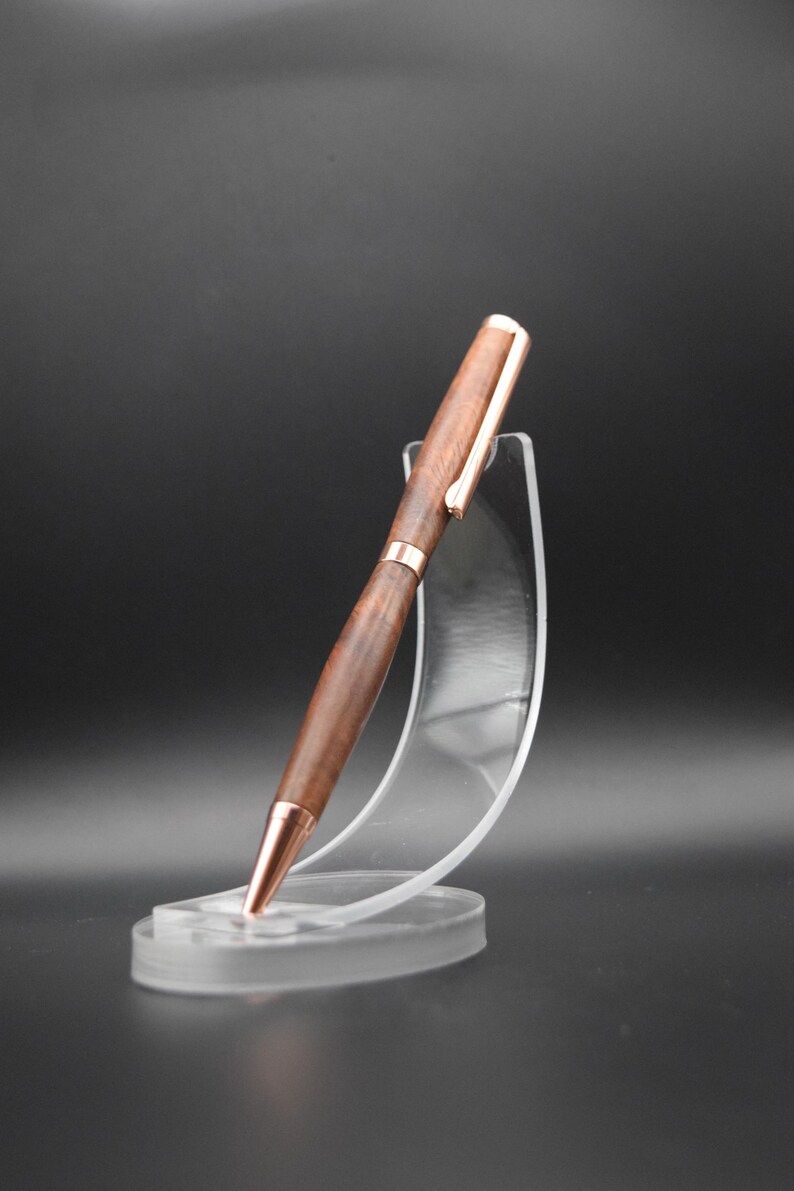 May include: A wooden pen with a rose gold finish and a clear plastic pen stand.