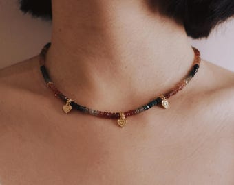 May include: A gold necklace with a multi-colored beaded chain and three small heart charms.