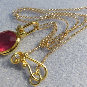 May include: A gold chain necklace with a pink gemstone pendant. The pendant is set in a gold bezel and has a small diamond accent.