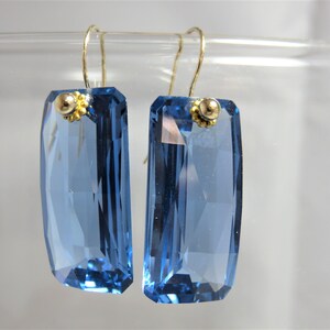 May include: A pair of blue crystal earrings with gold accents. The earrings are rectangular in shape and have a faceted design.