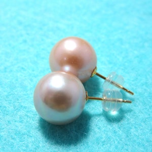 May include: A pair of pearl earrings with gold posts and clear plastic backs. The pearls are a light pink color.