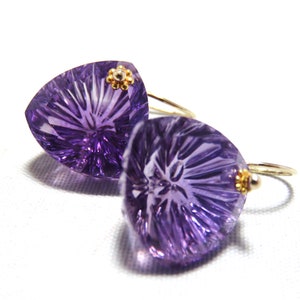 May include: A pair of amethyst earrings with a gold flower accent. The earrings are shaped like a triangle and have a faceted design.