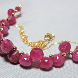 May include: A pink gemstone necklace with a gold chain. The necklace features faceted pink gemstones and gold beads.