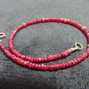 May include: A delicate necklace featuring a continuous strand of small, faceted, deep red gemstone beads. The strand is accented with tiny, evenly spaced gold-toned metal beads and finished with a gold-toned circular clasp and a spring ring closure.