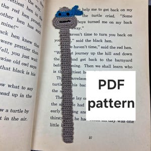 Pode incluir: Marcador de livros de crochê com um design das Tartarugas Ninja. O marcador é cinza com uma máscara azul e um rosto sorridente. O texto "PDF pattern" é visível na página.