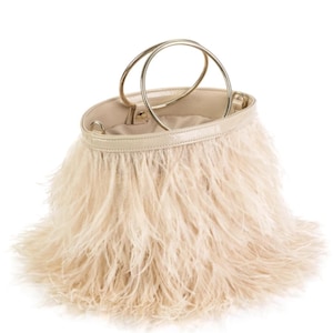 May include: A cream-colored handbag with a fluffy feather exterior. The bag has a circular gold-colored handle and a smooth, light-colored leather trim. The interior of the bag is a matching cream color.