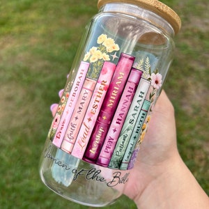 May include: A clear glass jar with a bamboo lid, featuring a colorful design of stacked books with the names of women from the Bible and their associated virtues. The text reads "Women of the Bible".