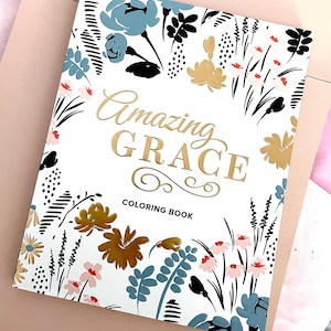 以下が含まれることがあります： 花柄と「Amazing Grace Coloring Book」の文字が金箔でデザインされた白い塗り絵の本です。
